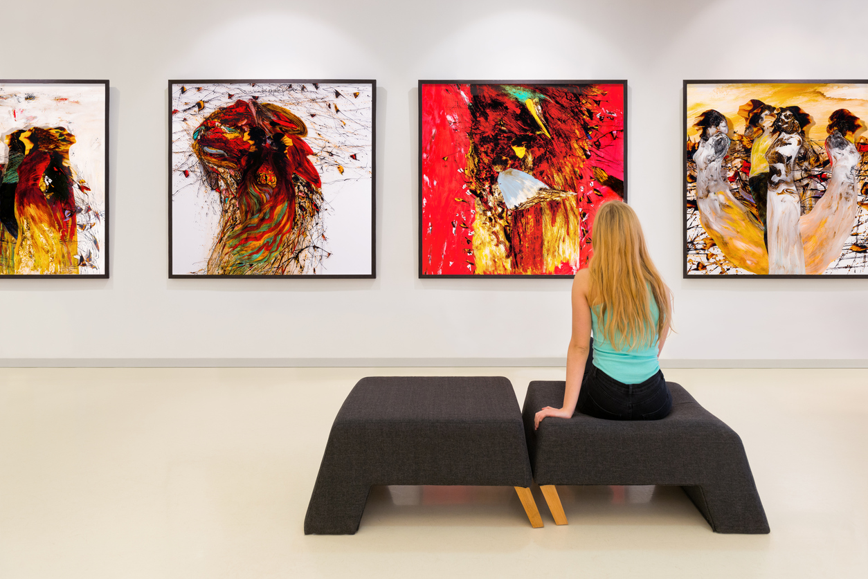 In a exhibition centre, lonely young woman visits an art exhibition and watches artist's collection on the wall. Exhibition's concept is "Angels"