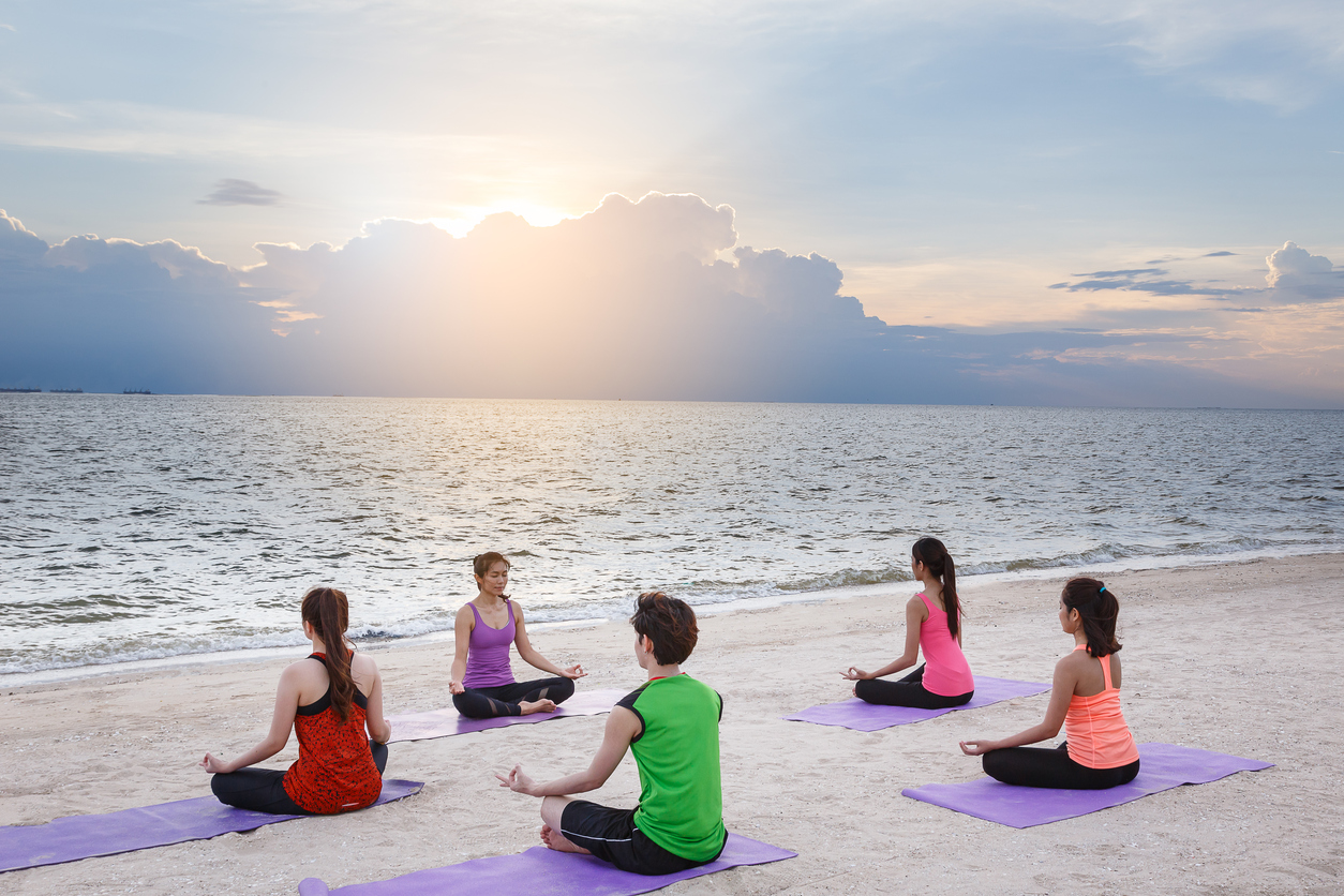 Group of young people practicing yoga on the beach, yoga and healthy lifestyle concept