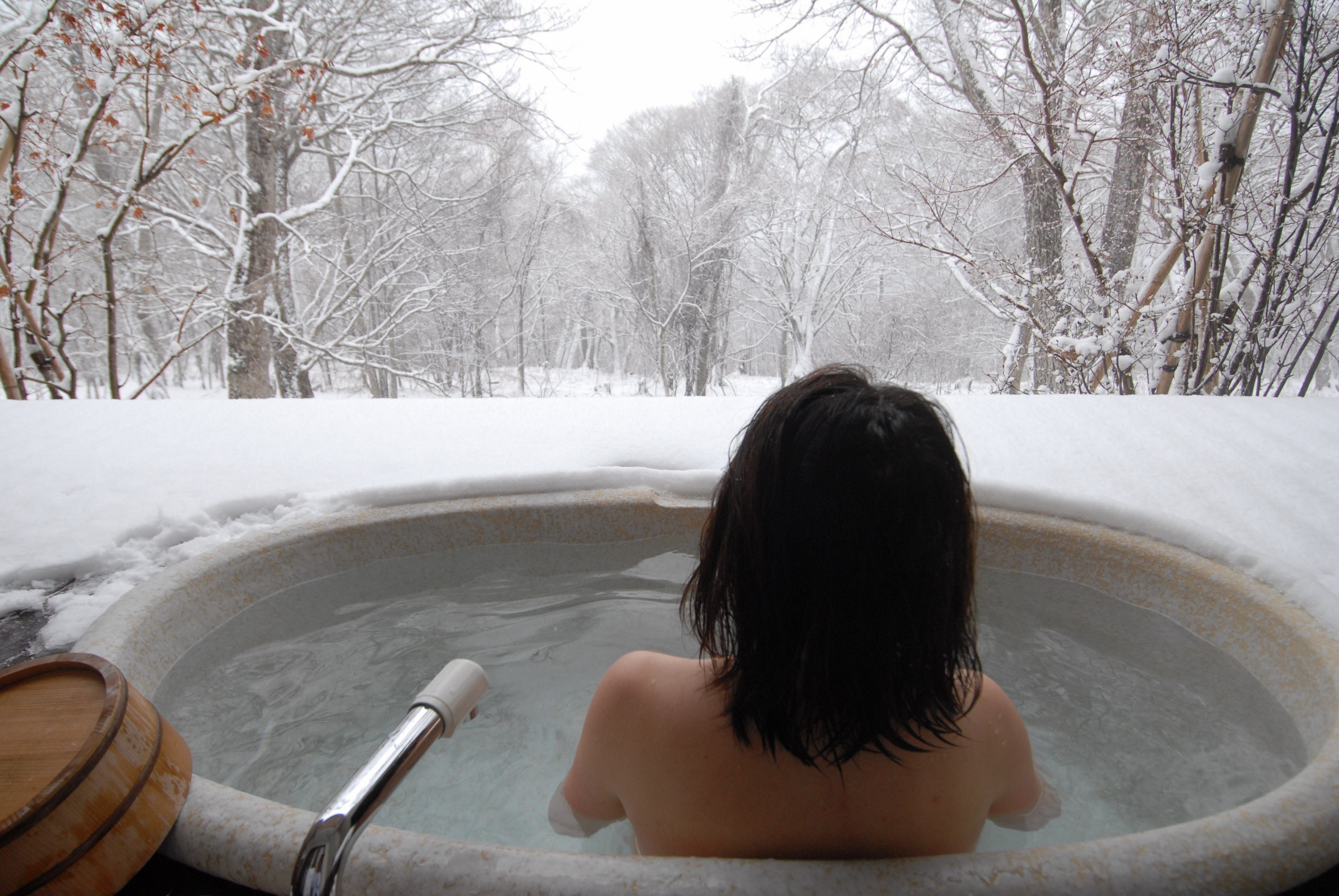 young Japanese woman in a hot open air bath while snowing