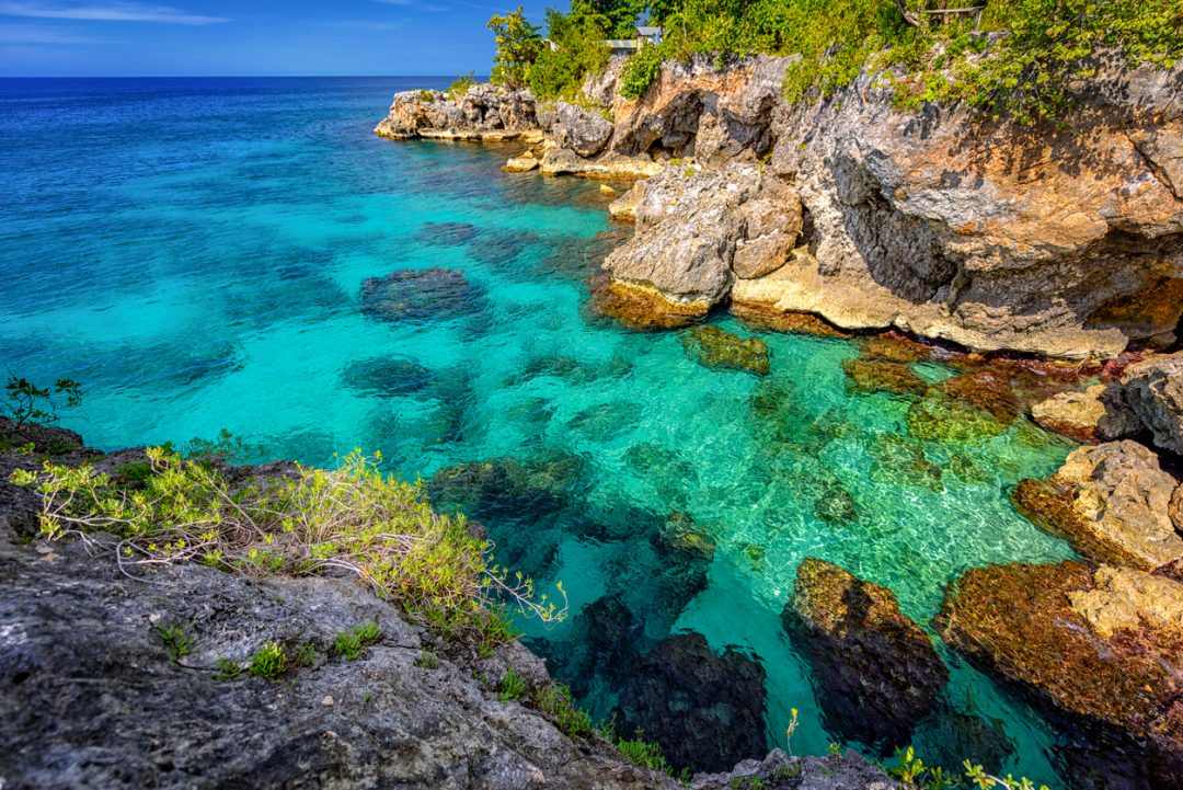 Beautiful clear turquoise water near rocks and cliffs in Negril Jamaica. Caribbean paradise island and water at the seaside with a blue sky and nice day light