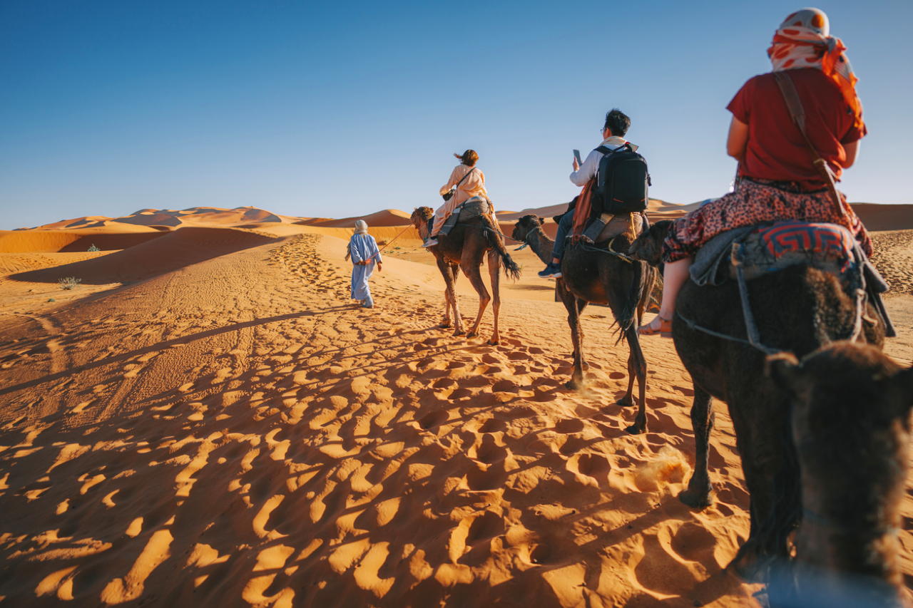 Gruppo di turisti su cammelli durante un tour nel deserto del Sahara in Marocco all'ora del tramonto